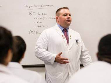 Attending physician lectures in front of white board.
