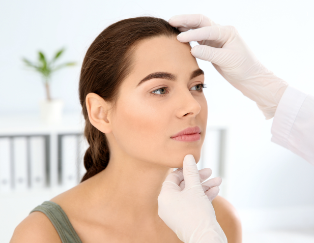 A woman's face is examined by an unseen provider wearing white gloves.